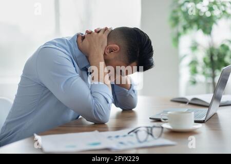 Junger arabischer Mann mit starken Nackenschmerzen oder Kopfschmerzen, müde von der Arbeit am Laptop im modernen Büro, Kopierraum Stockfoto