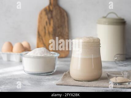 Aktiver Weizensauerteigstarter im Glasgefäß. Lebensmittelzutaten für den Teig. Küchenhintergrund. Horizontales Bild. Stockfoto