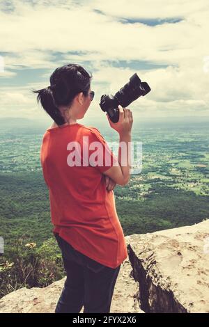 Ganzer Körper der asiatischen Frau mit Digitalkamera am Aussichtspunkt auf der Spitze des Berges, Reisen im Urlaub. Rückansicht einer Frau, die gegen den Himmel mit Kl Stockfoto