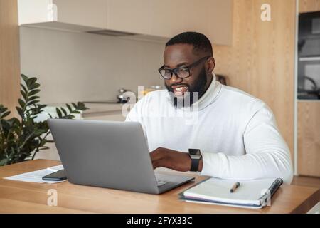 Lächelnder junger afro-amerikanischer Freiberufler, der online studiert oder arbeitet Auf einem Laptop Stockfoto