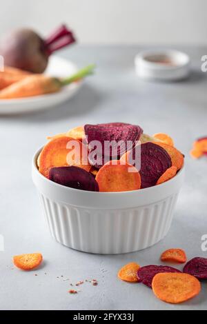 Schüssel mit gemischten gesunden Gemüsechips aus Rüben und Karotten auf grauem Hintergrund. Getrocknetes Gemüse. Vertikales Bild. Stockfoto