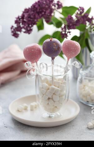 Leckere Kuchen knallt in einem Glas mit Marschmalchen auf einem Hintergrund von Fliederblumen. Vertikales Bild. Stockfoto