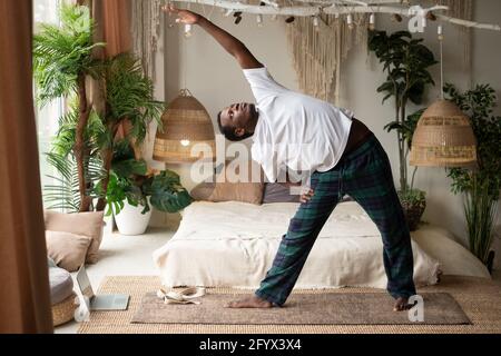 Afrikanischer Mann, der Yoga praktiziert, indem er trikonasana oder Triangle Pose tut Zu Hause Stockfoto