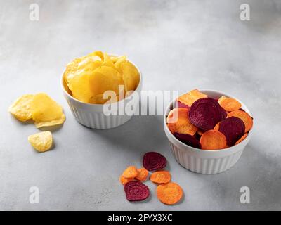 Leckere Kartoffeln, Karotten, Rübenchips in Schalen auf grauem Hintergrund. Veganes Alternativfutter. Horizontales Bild. Kopierraum. Stockfoto