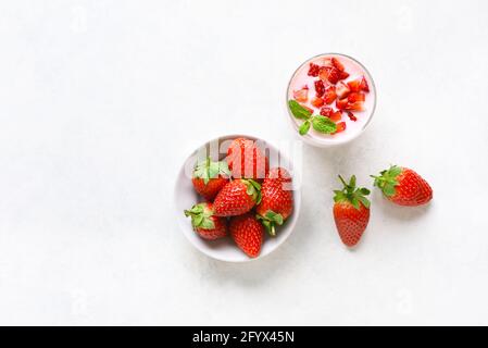 Erdbeerjoghurt mit frischen Beeren auf weißem Stein-Hintergrund mit freiem Textraum. Gesundes Lebensmittelkonzept. Draufsicht, flach liegend Stockfoto