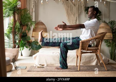 Afrikanischer Mann mit Stuhl in seinem Wohnzimmer zu Hause macht Yoga Asana für Anfänger. Stockfoto