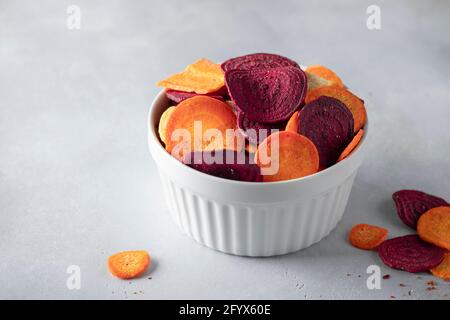 Volle Schüssel mit vegetarischen Chips aus Rüben und Karotten auf grauem Beton-Hintergrund. Vegane Ernährung. Horizontales Bild. Platz für Text Stockfoto