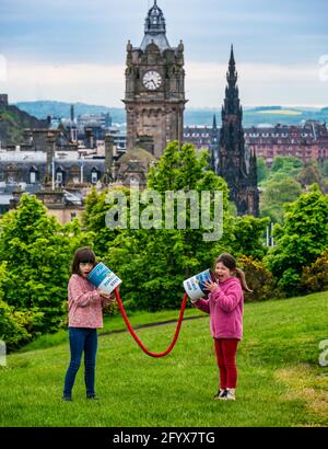 Zwei junge Mädchen geben vor, mit riesigen verbundenen Blechdosen zu kommunizieren und starten das Edinburgh Science Festival, Calton Hill mit der Skyline der Stadt, Schottland, Großbritannien Stockfoto