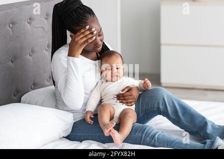 Müde afroamerikanische junge Mutter sitzt mit Kind auf dem Bett Stockfoto