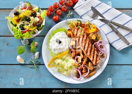Griechischer gemischter Grill mit Gyros, Souflaki, Tsatziki und Krautsalat, serviert mit einem Bauernsalat Stockfoto