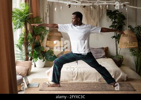 Afrikanischer junger Mann, der eine Kriegerpose oder Virabhadrasana B tut Zu Hause Stockfoto