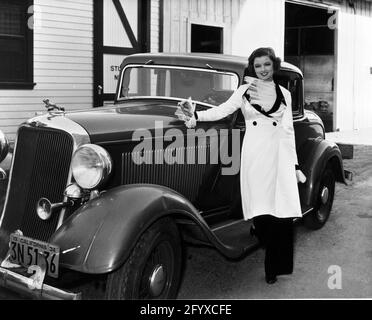 Die amerikanische Schauspielerin Myrna Loy (geb. Myrna Adele Williams; 1905 - 1993), gekleidet in ein Outfit von 'The Thin man', steht um 1934 in einem Filmstudio neben einem Auto. (Foto von Burton Holmes) Stockfoto