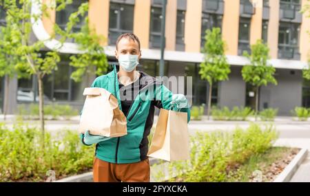 Postlieferer Kurier Mann trägt schützende Gesichtsmaske vor Von Transportwagen, der aufgrund des Coronavirus Pakethaltekasten liefert Krankheit oder COVID-19 Stockfoto