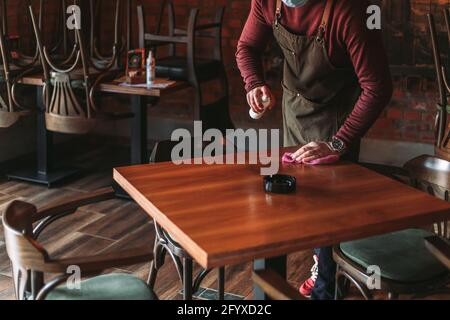 Junger Kellner, der Tisch im Café desinfiziert. Coronavirus-Konzept Stockfoto