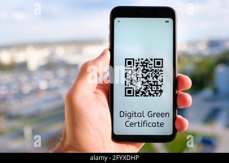 Digitales Green Certificate mit QR-Code auf dem Bildschirm des Mobiltelefons in mans Hand auf dem Hintergrund des Stadtbildes. Stockfoto