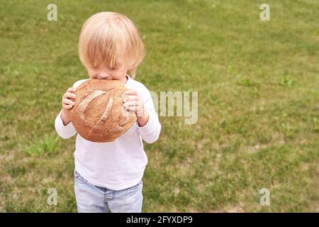 Kind hält und beißt rundes Brot. Gesunde Ernährung Stockfoto