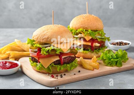 Hausgemachte Burger mit Rindfleisch, Käse und Gemüse auf grauem Hintergrund. Seitenansicht, horizontal. Stockfoto