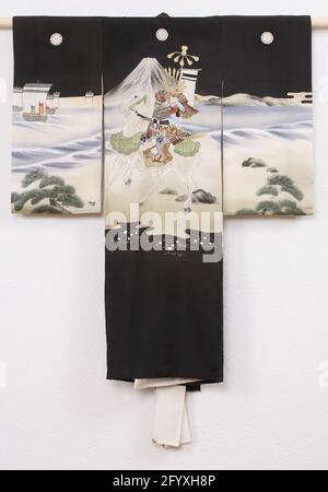 Jungen Miyamairi Kimono mit der Schlacht am Fuji River. Formeller Kimono für einen Jungen beim ersten Besuch eines schintoistischen Schreines (Miyamairi Kimono), mit einer Dekoration einer nächtlichen Szene mit einem Samurai zu Pferd am Ufer des Fuji-Flusses, dem Berg und Schiffen im Hintergrund. Wahrscheinlich eine Szene aus der Schlacht am Fuji im Jahr 1180. Schwarze Seide mit einer bemalten yuzen-Dekoration mit bestickten Details und Goldfolie. Weißes Seidenfutter. Fünf Familienwaffen (Mon) von Klazuring (Katabami). Stockfoto