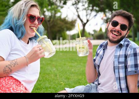 Zwei Freunde lachen und trinken erfrischende Getränke im Park beim Picknick an einem sonnigen Sommertag. Stockfoto