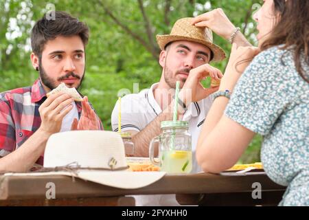 Eine Gruppe von glücklichen Freunden, die Spaß haben, Sandwiches trinken und essen in einem Park. Picknick an einem sonnigen Sommertag. Stockfoto