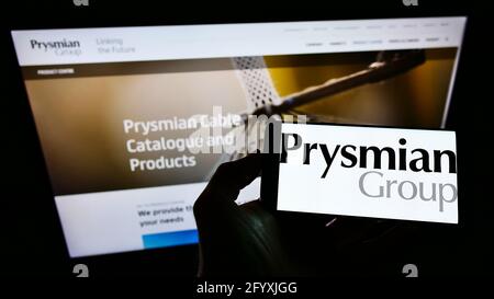 Person, die das Mobiltelefon mit dem Logo des italienischen Elektrokabelherstellers Prysmian Spa auf dem Bildschirm vor der Webseite hält. Konzentrieren Sie sich auf die Telefonanzeige. Stockfoto