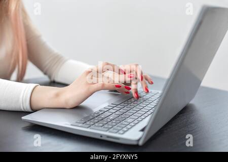 Selektiver Weichfokus schöne weibliche Hand tippen Text auf der Laptop-Tastatur. Leuchtend rote Maniküre. Konzept der Arbeit im Büro von Geschäftsfrau und com Stockfoto