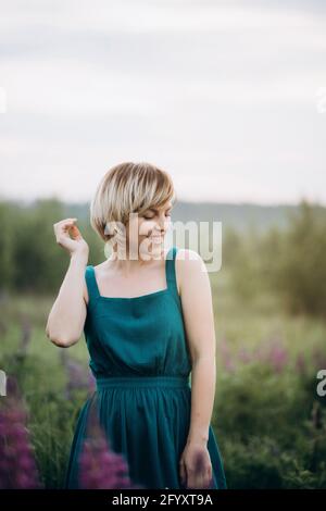 Ein schönes Mädchen in einem blauen Kleid in einem Feld von Lupinen Blumen tanzt und lächelt. Vertikal Stockfoto