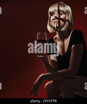 Porträt einer erschöpften, hübschen Blondine, die Wein trinkt und raucht Stockfoto