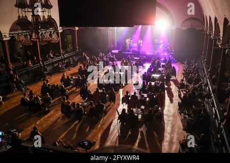 Leipzig, Deutschland. Mai 2021. Konzertbesucher sitzen in einem Konzert des Musikers Fil Bo Riva im Felsenkeller. Hier findet nach eigenen Angaben das erste Indoor-Konzert im Jahr 2021 deutschlandweit statt. Die Halle war mit Stühlen und Tischen eingerichtet und eineinhalb Meter voneinander entfernt. Masken waren überall obligatorisch, außer an ihrem eigenen Platz. Quelle: Jan Woitas/dpa-Zentralbild/dpa/Alamy Live News Stockfoto