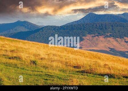Ländliche Landschaft mit Feldern auf Hügeln. Gebirgige Naturlandschaft im Sommer bei Sonnenaufgang. Glühende Wolken über dem Bergrücken in der Ferne Stockfoto
