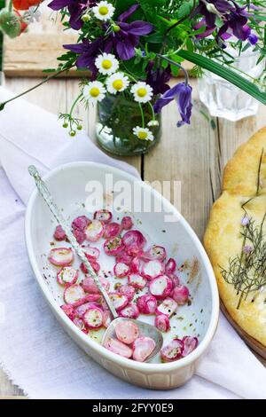 Focaccia mit Zwiebeln, gebackenem Rettich und einem Blumenstrauß auf einem Holztisch. Stockfoto