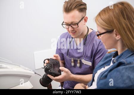 Männlicher Zahnarzt zeigt seine Patienten Fotos von ihren Zähnen danach Zahnbehandlung Stockfoto