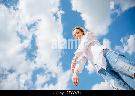 Ansicht der schönen Frau in weißem Hemd und Jeans mit Löchern, mit blau bewölktem Himmel. Stockfoto