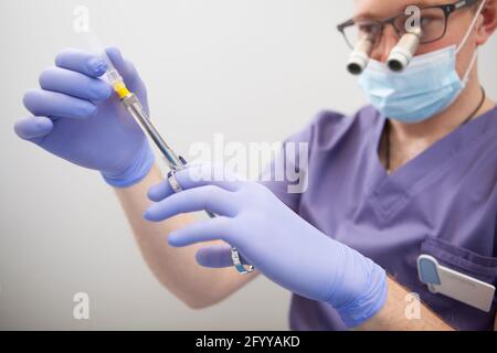 Nahaufnahme eines männlichen Chirurgen mit einer Anästhesiespritze und einer Mikroskopbrille Stockfoto