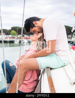 Seitenansicht eines lächelnden multirassischen Paares, das sich küsst, während die Augen geschlossen sind Auf der Yacht im Stadthafen Stockfoto