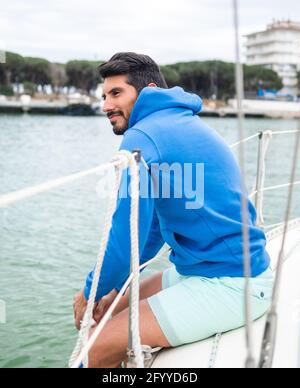 Seitenansicht eines lächelnden ethnischen Mannes im Kapuzenpullover, der die Wellen bewundert see vom Motorboot aus, während man in die Stadt blickt Stockfoto