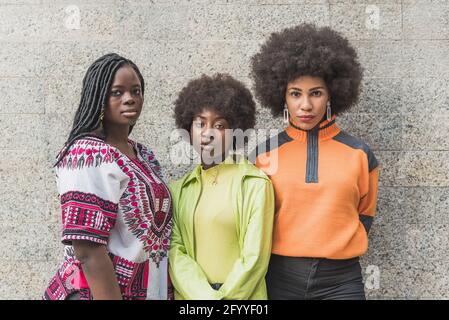Junge selbstbewusste beste ethnische afroamerikanische Freundinnen suchen Bei der Kamera auf grauem Hintergrund im Freien Stockfoto
