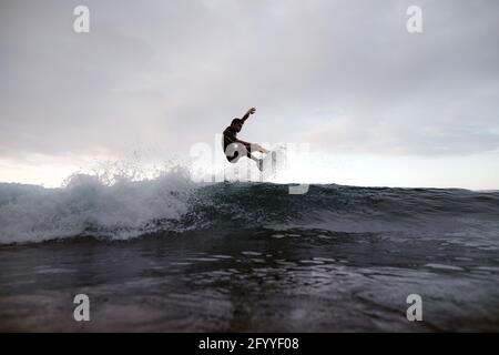 Junger Surfer auf dem Surfbrett übt Extremsport auf dem Meer aus Winken Sie unter bewölktem Himmel Stockfoto