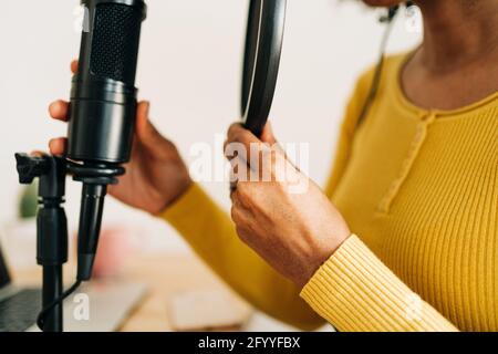 Beschnitten unkenntlich junge schwarze Frau in legerer Kleidung Aufnahme Podcast Sitzen am Tisch mit Laptop und Mikrofon im hellen Studio Stockfoto