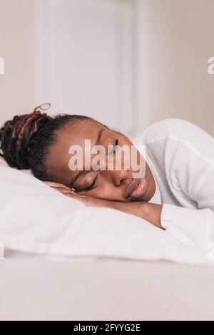 Junge afroamerikanische Frau Millennial mit dunklem Haar in Casual Die Kleidung liegt auf einem weichen Bett und schläft am sonnigen Morgen Zu Hause Stockfoto