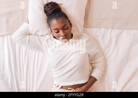 Junge afroamerikanische Frau Millennial mit dunklem Haar in Casual Die Kleidung liegt auf einem weichen Bett und schläft am sonnigen Morgen Zu Hause Stockfoto