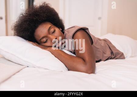 Junge afroamerikanische Frau Millennial mit dunklem Haar in Casual Die Kleidung liegt auf einem weichen Bett und schläft am sonnigen Morgen Zu Hause Stockfoto