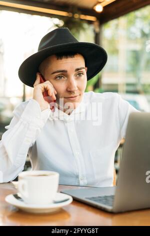 Stilvolle freiberufliche Mitarbeiterin, die während der Arbeit im Café telefoniert Mit Laptop und einer Tasse Kaffee Stockfoto