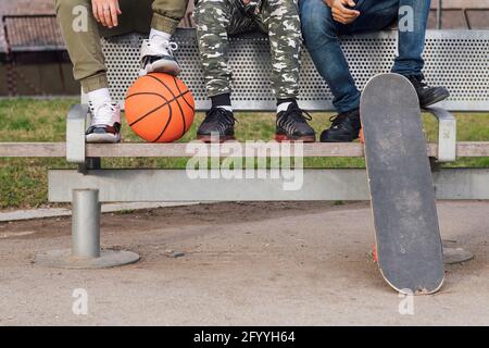 Ernte von multirassischen männlichen Freunden sitzen auf Bank mit Basketball Und Skateboard und aufmerksam wegschauen Stockfoto