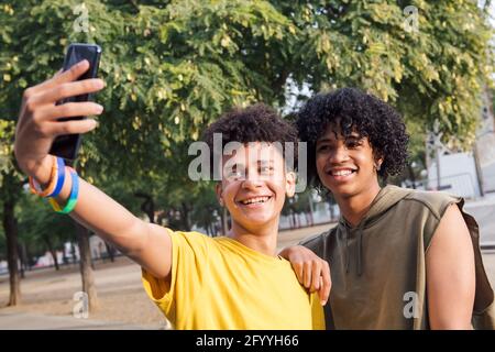 Entzückend schwarze männliche Teenager stehen unter Baum und nehmen sich selbst. Porträt auf Handy im Park Stockfoto