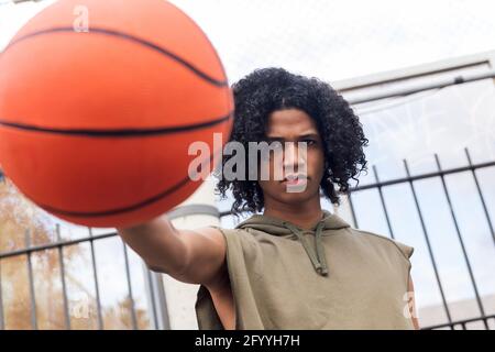 Niedriger Winkel des ernsten afroamerikanischen Teenagers mit Afro Frisur wirft Basketball während des Trainings im Park Stockfoto