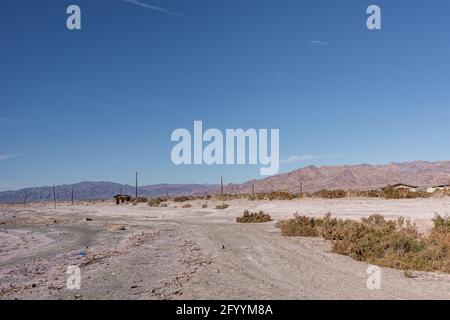 USA, CA, Salton Sea - 28. Dezember 2012: Weißgrauer salziger Sand der Küste SE in der Nähe von Niland Marina mit Wohnhäusern hinten unter blauem Himmel und Stockfoto