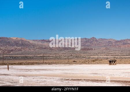 USA, CA, Salton Sea - 28. Dezember 2012: SE-Küste mit kleiner ruinöser Hütte isoliert am Wtie-Strand mit Bergen am Horizont und blauem Himmel darüber. Stockfoto