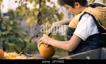 Junge schnitzt Kürbisse für halloween im Hinterhof. Lustige Familienaktivitäten. Stockfoto