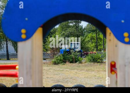 Unschärfe-blauen Traktor auf der Straße auf Baum Natur Hintergrund fahren. Rahmen aus Spielzeughaus auf Spielplatz. Ländliche Gegend. Nicht fokussiert. Stockfoto